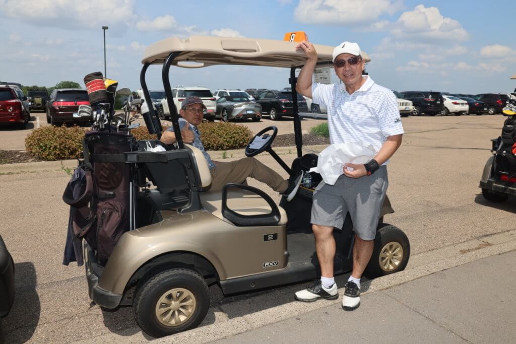 Golfer standing by golf cart, while his partner sits down, at 4th Annual Bridges to Learning Golf Tournament at The Wilds Golf Club, Prior Lake Minnesota. Raising funds to educate and care for poor children in Vietnam.