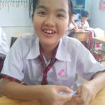 Young girl smiles at camera as she sews a button at school. Providing education to impoverished children in Vietnam.