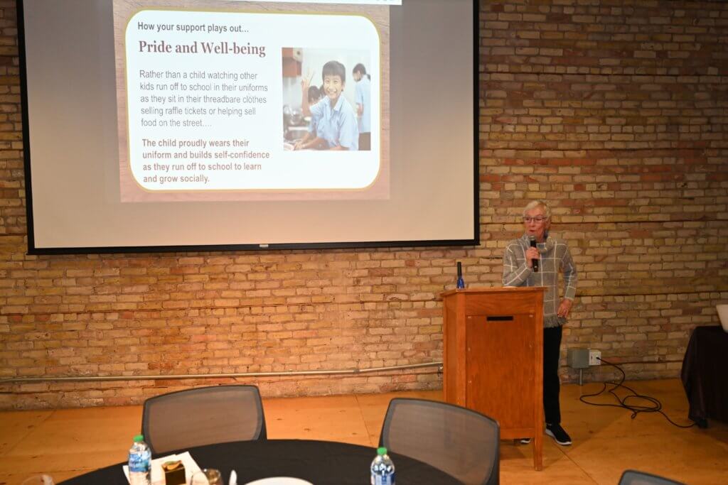 Bridges to Learning Founder holds the mic by the podium and thanks the guests. 2022 Wine Tasting to raise funds for poor children in Vietnam. Nonprofit.