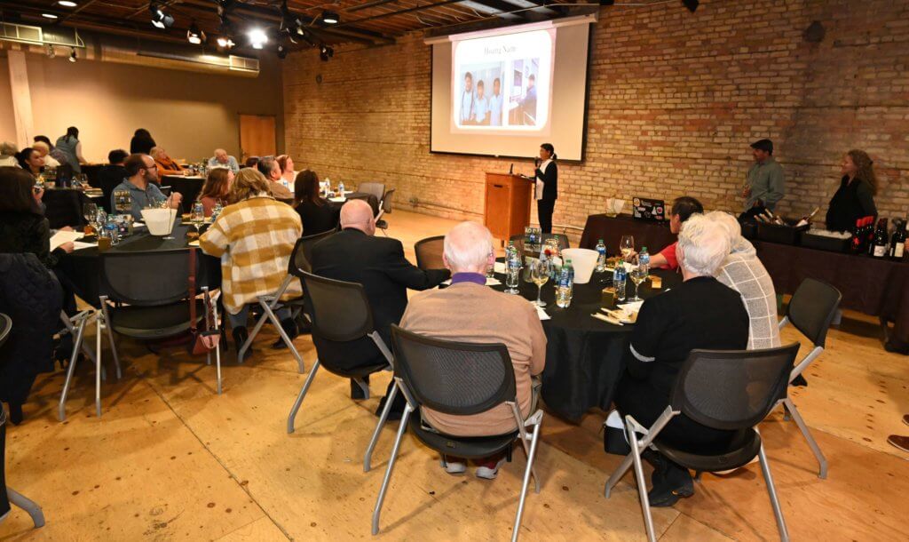 Seated 2022 Wine Tasting guests listen to wine expert, while enjoying food and wine. Bridges to Learning, Minnesota nonprofit.