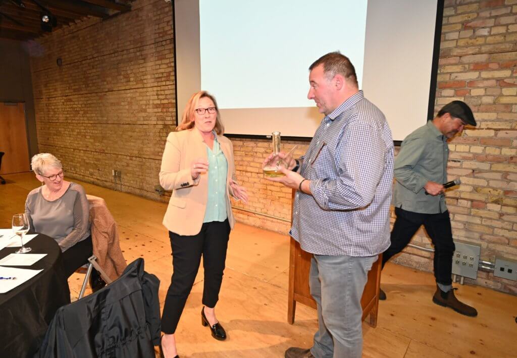 Bridges to Learning 2022 Wine Tasting guest learns how to use the porron. South Lyndale Liquors provides instruction. Nonprofit raising funds to educate poor children in Vietnam.