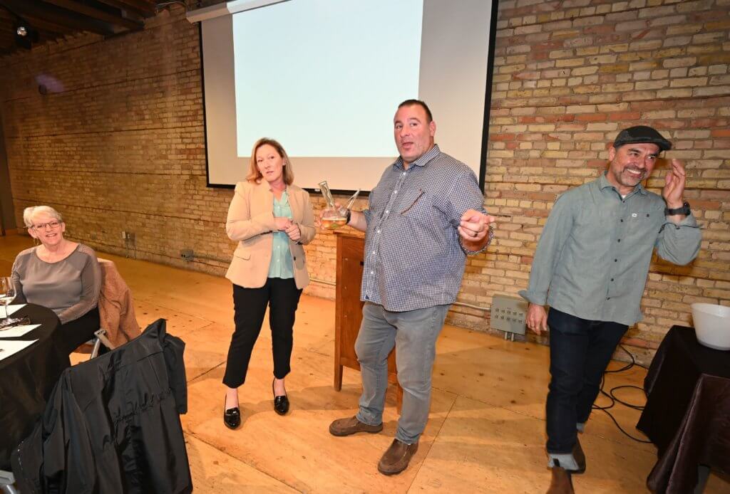 Bridges to Learning 2022 Wine Tasting guest learns how to use the porron. South Lyndale Liquors provides instruction. Nonprofit raising funds to educate poor children in Vietnam.