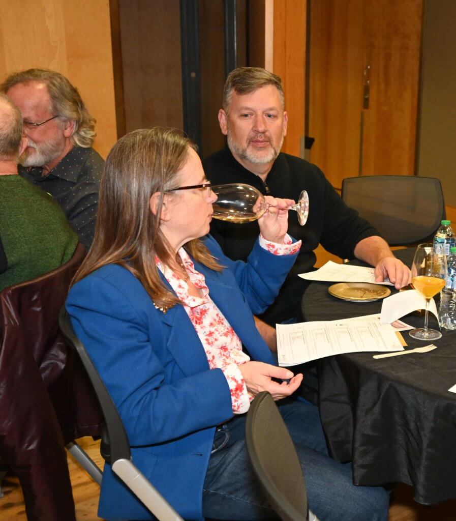 2022 Wine Tasting guest tastes white wine while another looks on at nonprofit Bridges to Learning event. Raising money to help educate poor children in Vietnam.