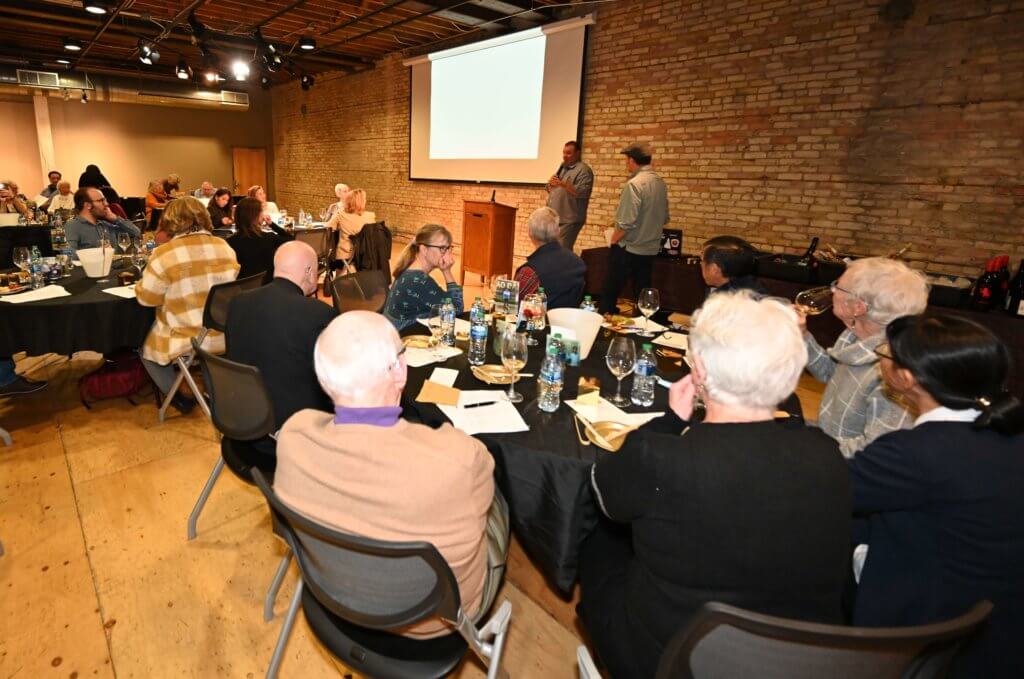 Guests at tables listen to Rootstock Wine Tasting introduce a wine at the Bridges to Learning 2022 Wine Tasting. Raising money to educate poor children in Vietnam.