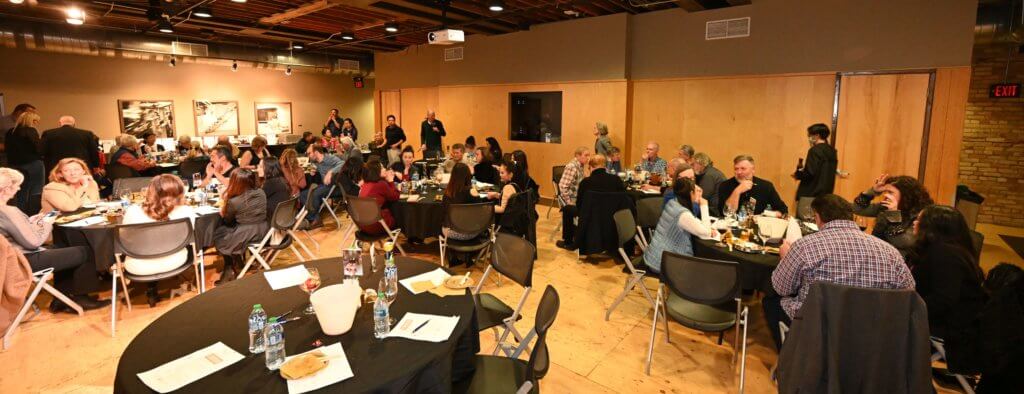 2022 Wine Tasting guests listen to Rootstock Wine Co. owner introduce a type of wine. Bridges to Learning nonprofit fundraiser. Minneapolis Minnesota.