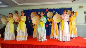 Girls in white ao dai dancing with hats. Celebration at Anh Linh School Saigon HCMC Vietnam.