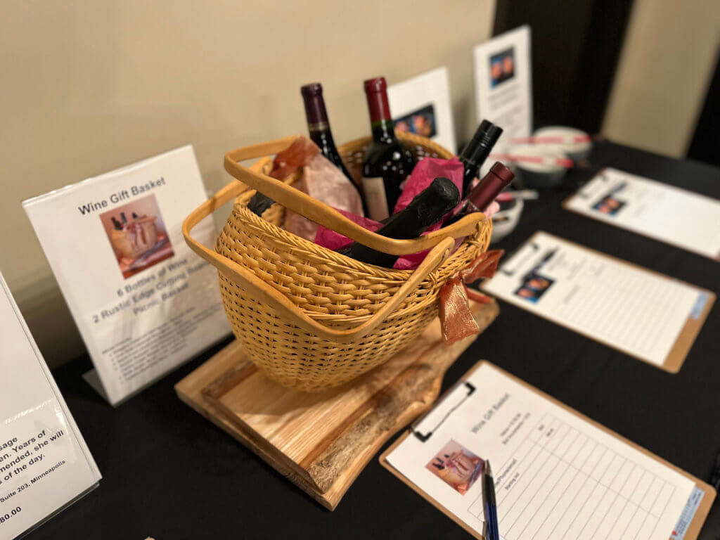 Table with items for the silent auction at the 2023 Bridges to Learning Wine Tasting fundraiser. Nonprofit raising funds to educate and nourish poor children in Vietnam. South Lyndale Liquors event space.