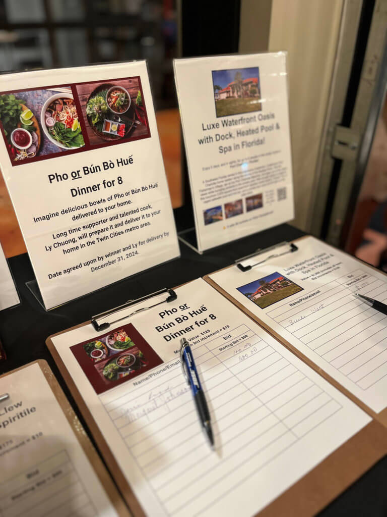 Table with items for the silent auction at the 2023 Bridges to Learning Wine Tasting fundraiser. Nonprofit raising funds to educate and nourish poor children in Vietnam. South Lyndale Liquors event space.