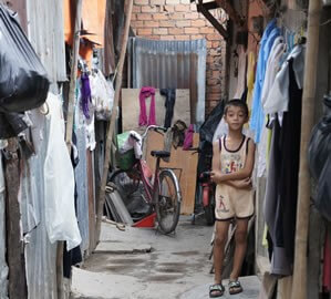 Young boy standing outside of his dilapidated home